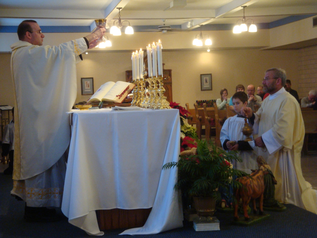 Father Joel elevates the chalice, with the Deacon Tom offering incensation.